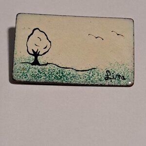 Scenic brooch featuring a tree, grass and birds.